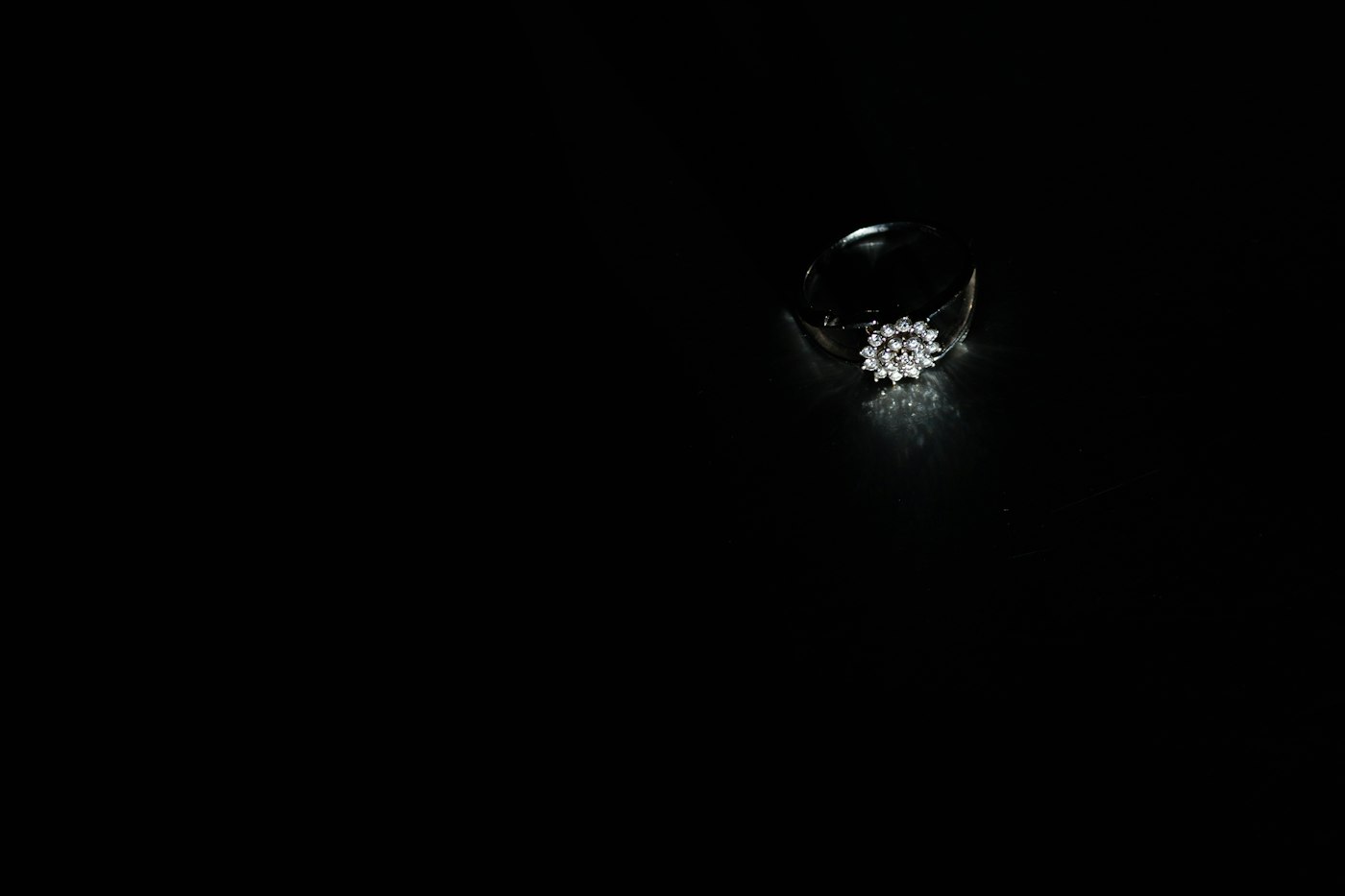 Inel cu diamante fotografiat singur, pe fundal negru, luminat de un fascicul dramatic de lumină